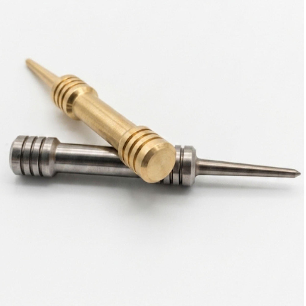 Brass and stainless steel barbell divot tools crossed, showing grooved grip rings and tapered single prong