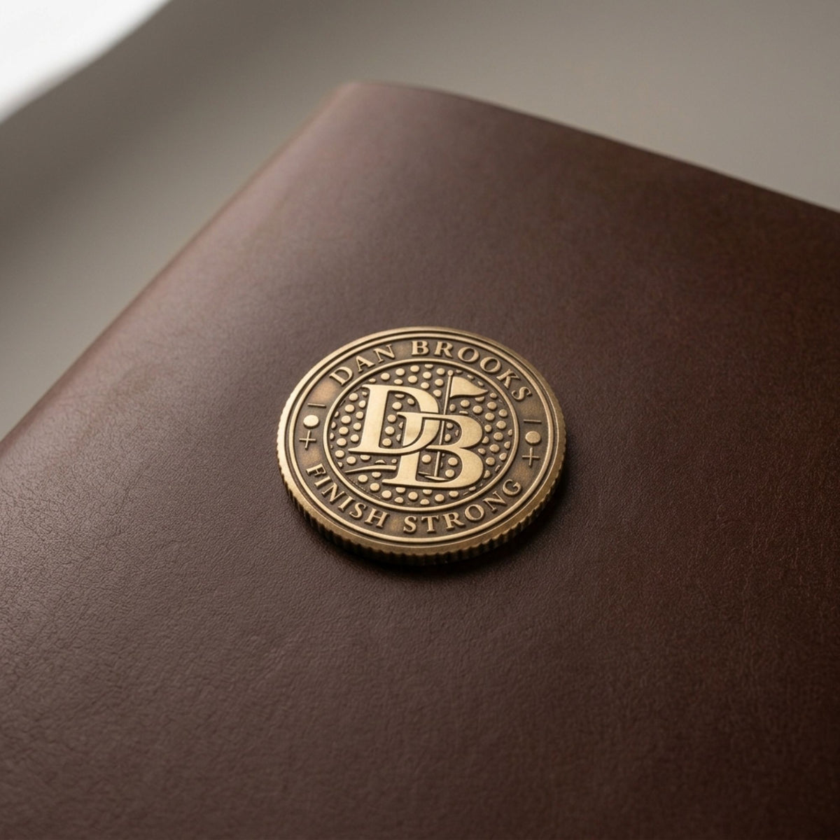 Monogrammed brass ball marker resting on a brown leather case