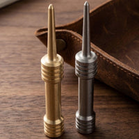 Brass and stainless steel barbell single prong divot tools standing on a wood table beside a leather tray