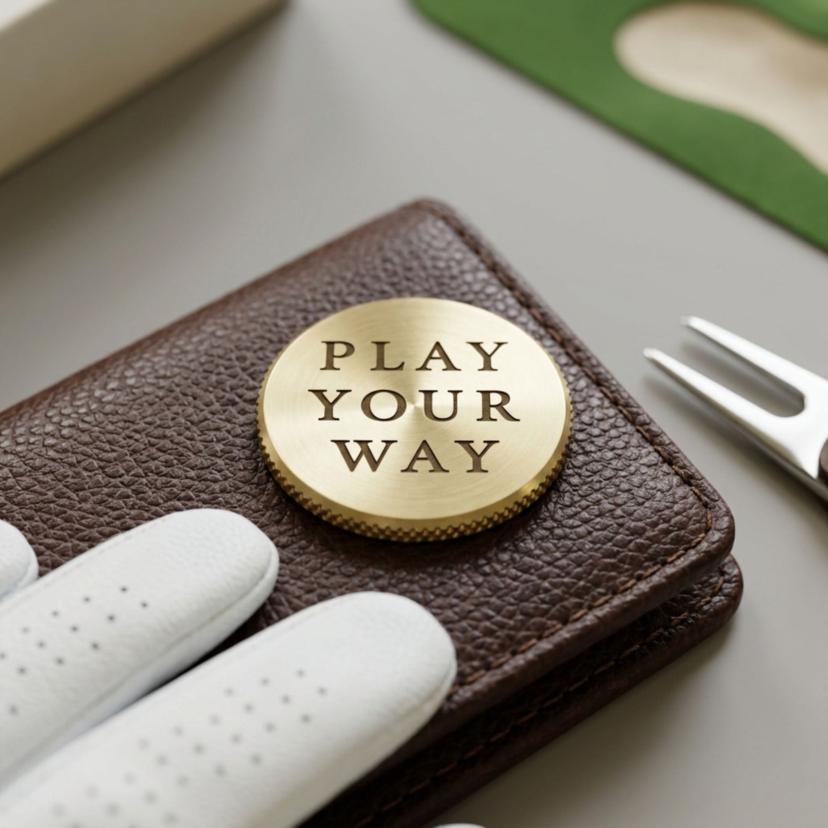 Brass ball marker engraved Play Your Way on a leather case with a white golf glove